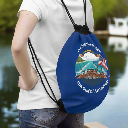 Drawstring bag featuring “I’ve Been Fishing the Gulf of America” text, placed on a wooden dock with Gulf waters and fishing gear in the background