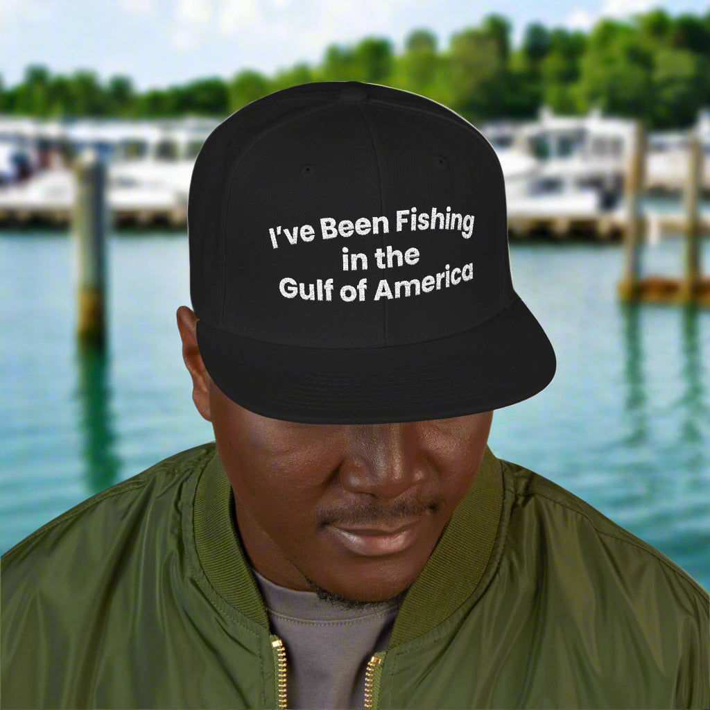Embroidered snapback cap reading “I’ve Been Fishing the Gulf of America” resting on a boat deck with Gulf waters in the background
